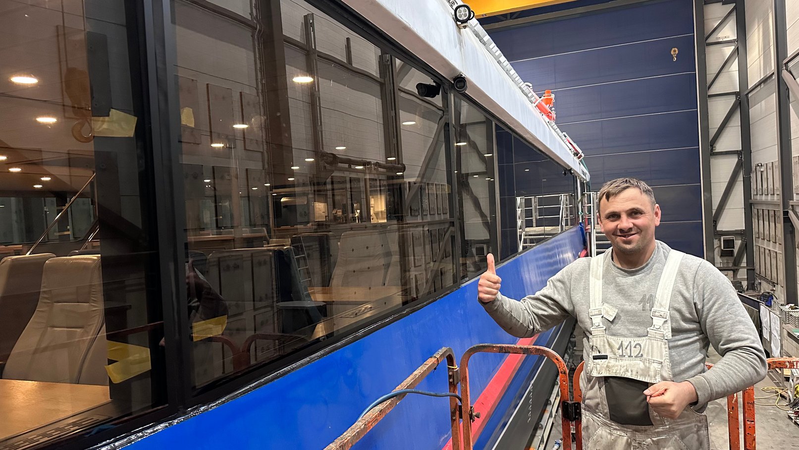Legal Composite Workforce technician working on a vessel hull in a shipyard hall